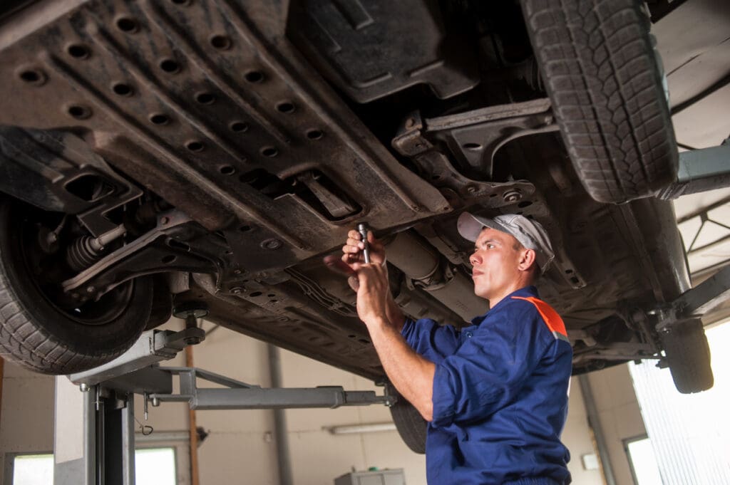 A mechanic uses an automotive lift to work on a vehicle in a maintenance shop.